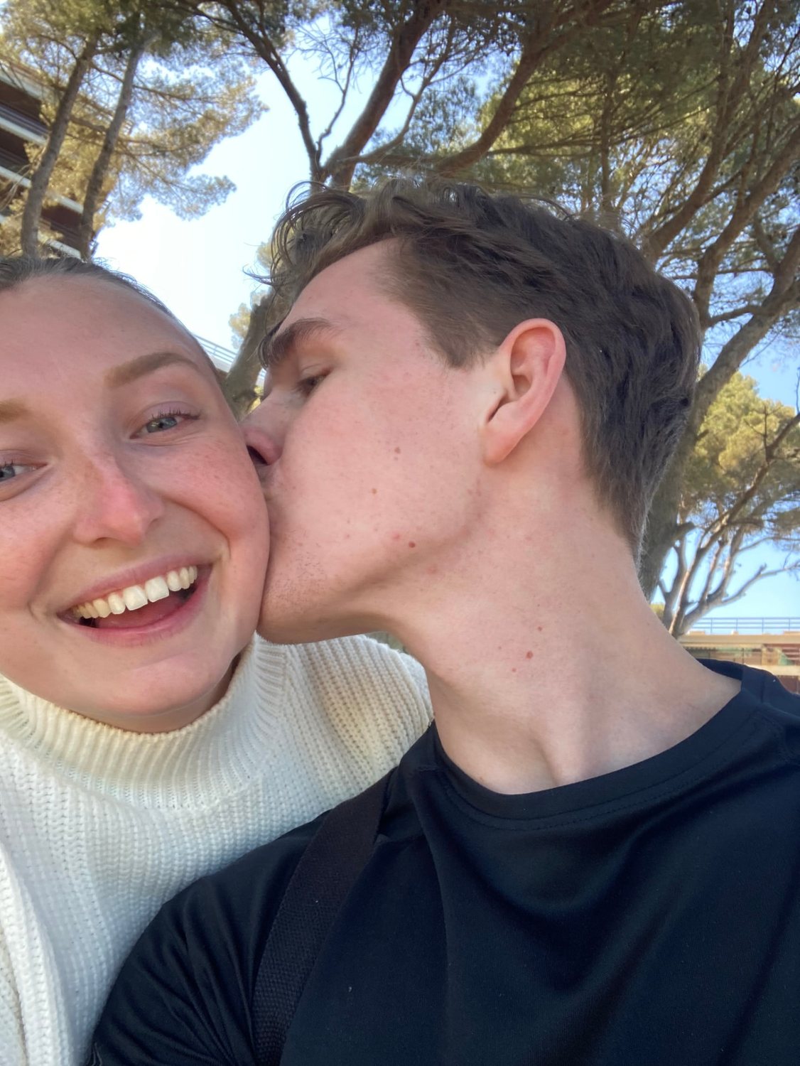 Filip och Josefin pussar varandra utomhus under pinjeträd