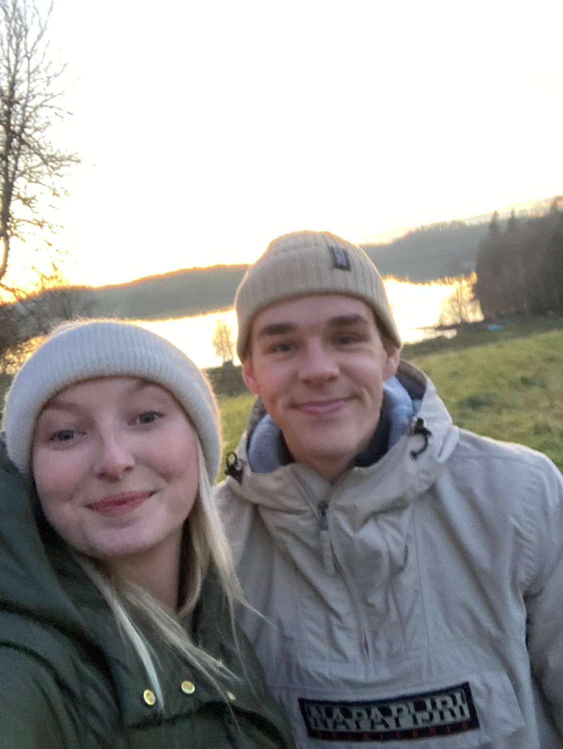 Filip och Josefin i mössor vid en sjö i solnedgången